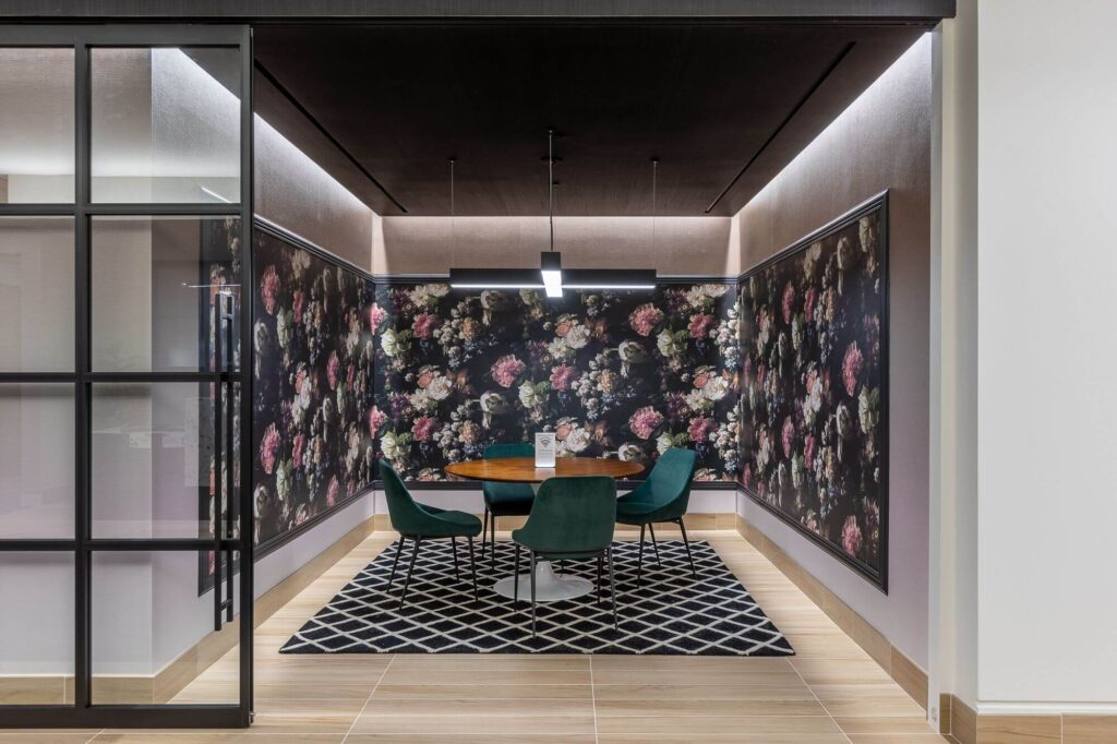 An office with glass-wall meeting rooms and floral wallpaper.